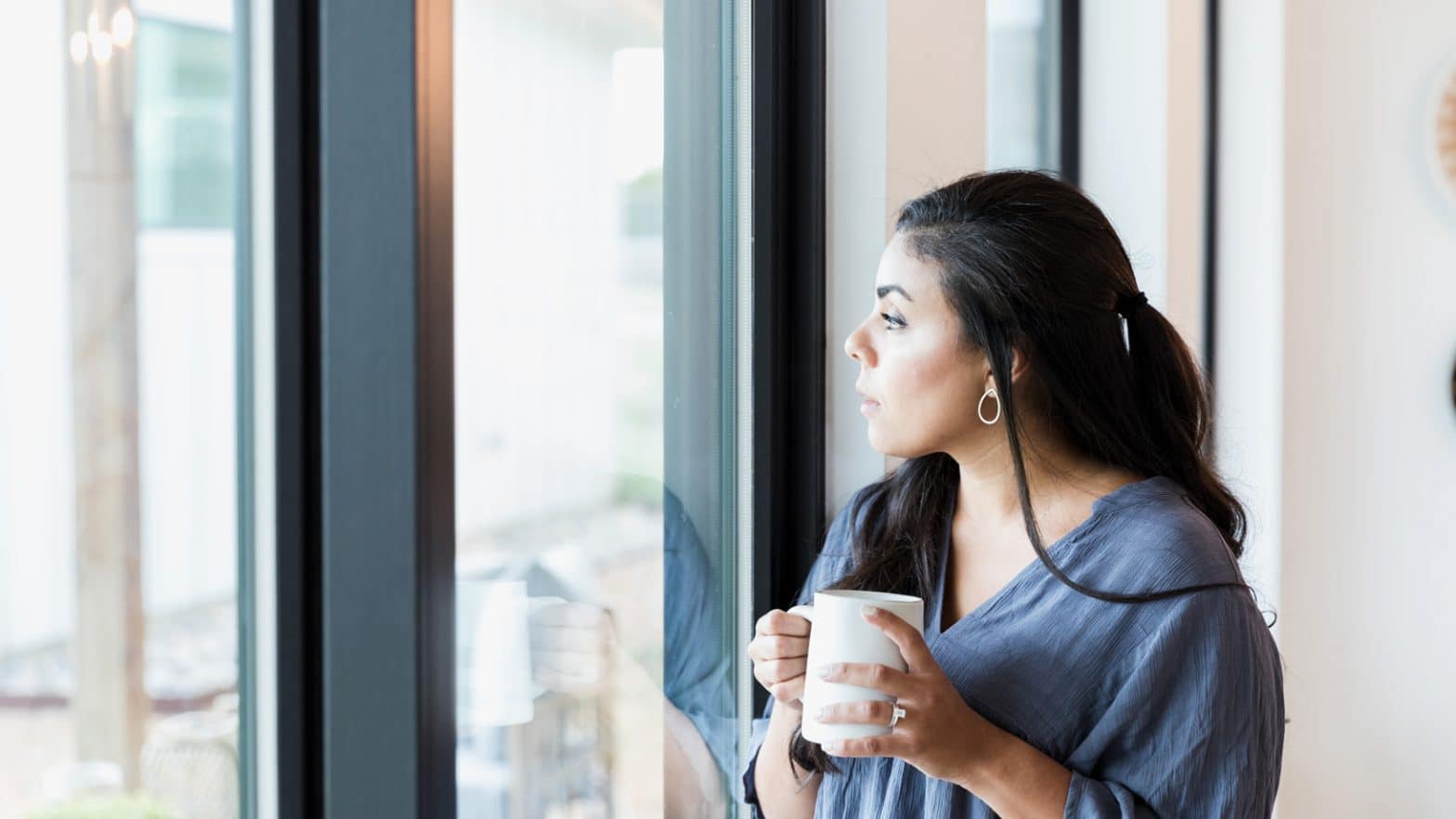 woman holding coffee and looking out the window