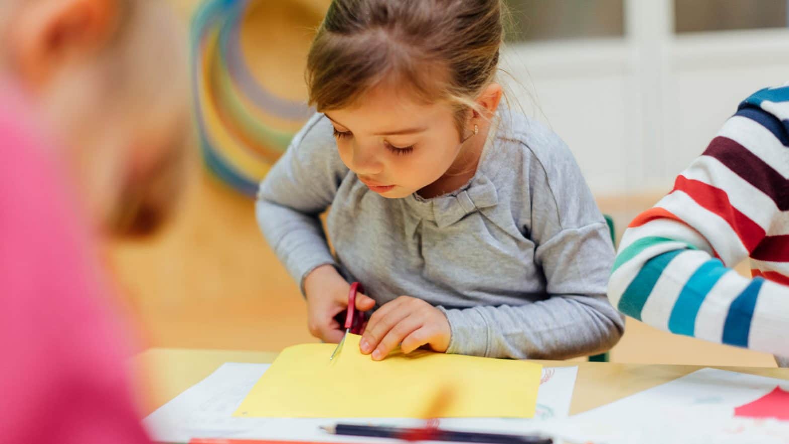 Happy Little Girl using scissors in kindergarten.