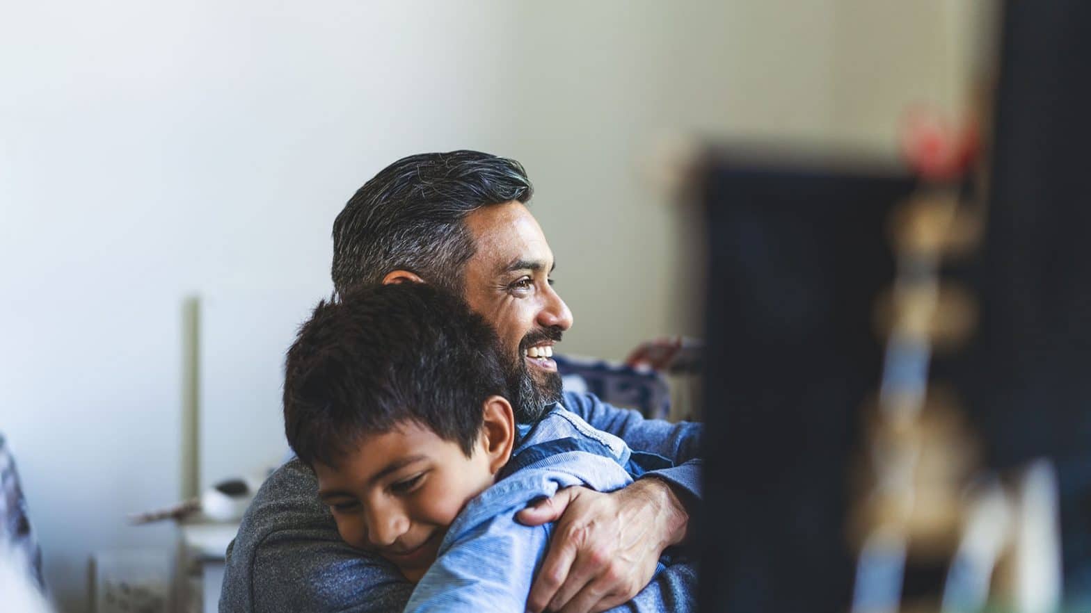 Smiling man embracing son in bedroom at home