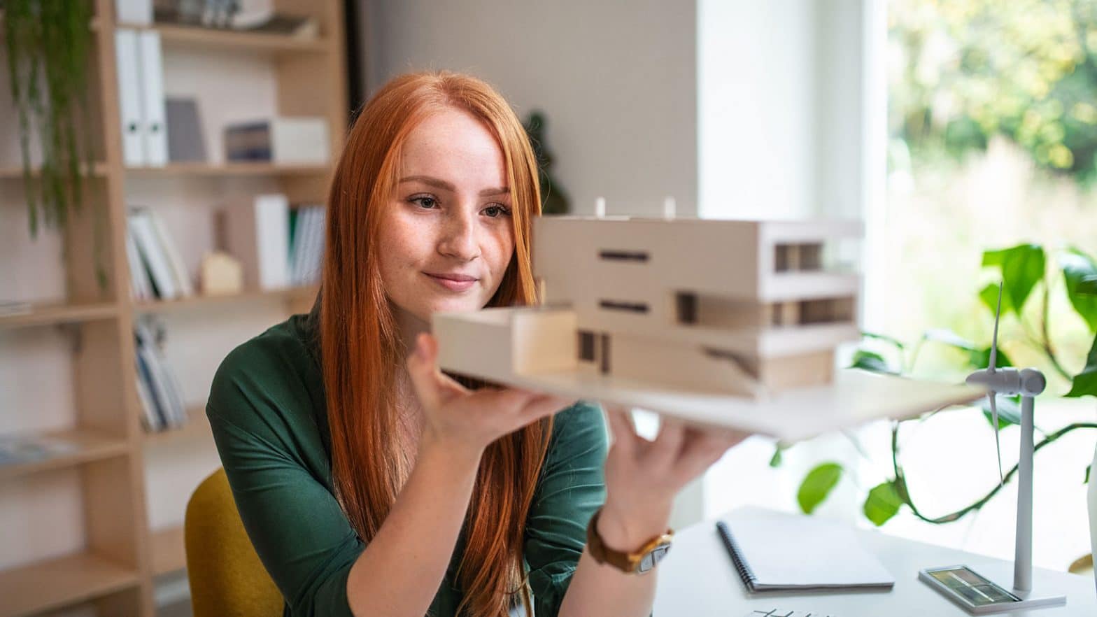 Architect with model of a house sitting at the desk indoors in office.