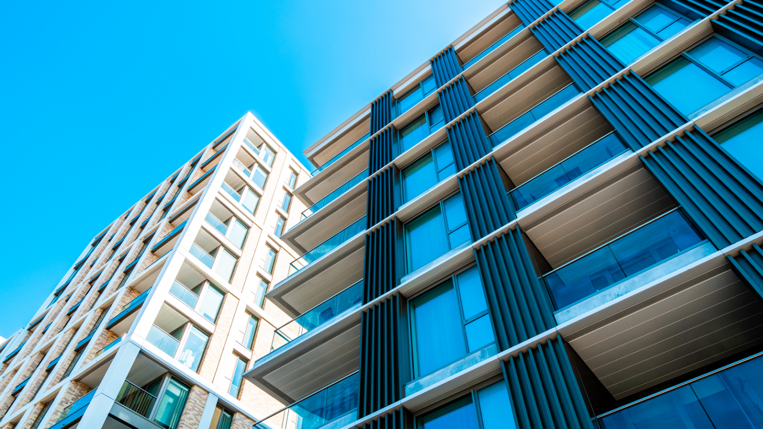 Modern high-rise apartment buildings with glass balconies and vertical panel details against a clear blue sky.