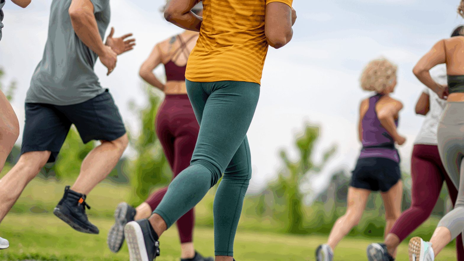 Several adults in athletic clothing are running on grass in Kent, with trees behind—perfect for B Corp team bonding.